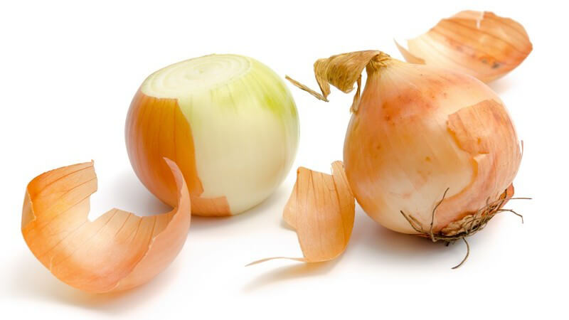 Geschälte und ungeschälte Speisezwiebel vor weißem Hintergrund