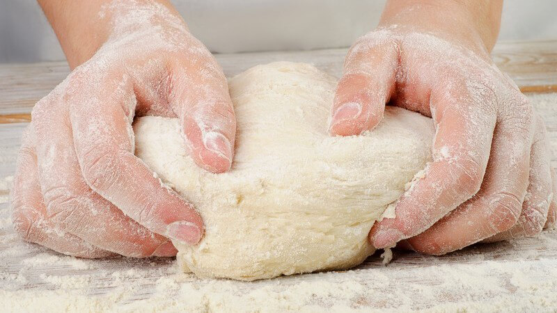 Hände kneten Teig in Mehl