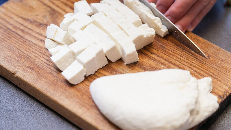 Indischer Frischkäse (Panir/Paneer) wird auf einem Holzbrett in kleine Stücke geschnitten