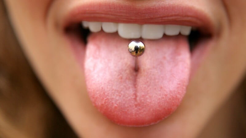 Frau steckt die Zunge raus, in der sich ein Barbell-Zungenpiercing befindet