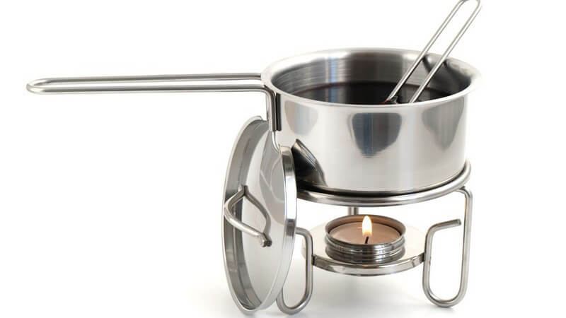 Kleiner Topf mit Glühwein wird über Teelicht erhitzt, weißer Hintergrund