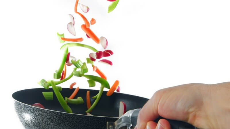 Frisches Gemüse wird in Pfanne umgedreht, weißer Hintergrund