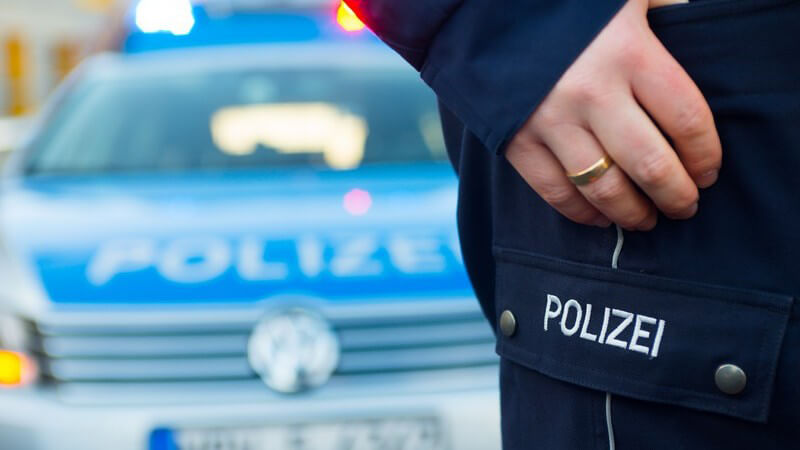 Ausschnitte eines Polizisten, im Hintergrund Polizeiauto, Fahrzeugkontrolle
