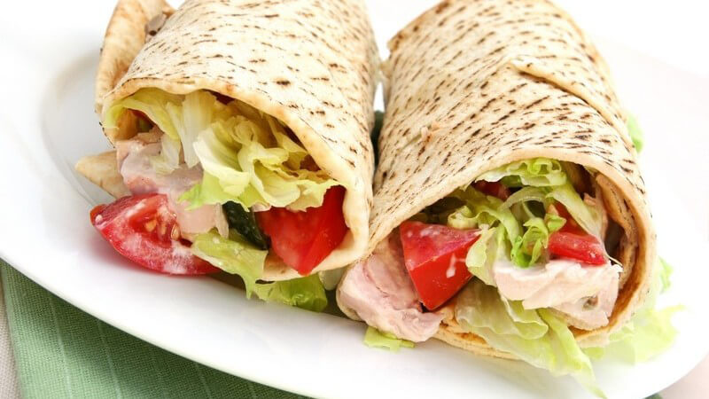 Zwei Wraps mit buntem Salat und Hühnchenfleisch auf weißem Teller