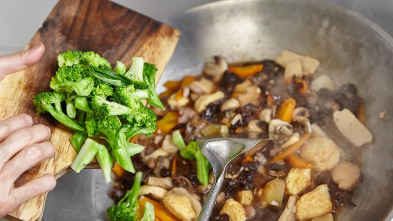 Brokkoli-Röschen werden von einem Holzbrett in den Wok gegeben