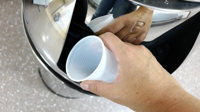 Hand wirft einen Plastikbecher in einen Push-Mülleimer