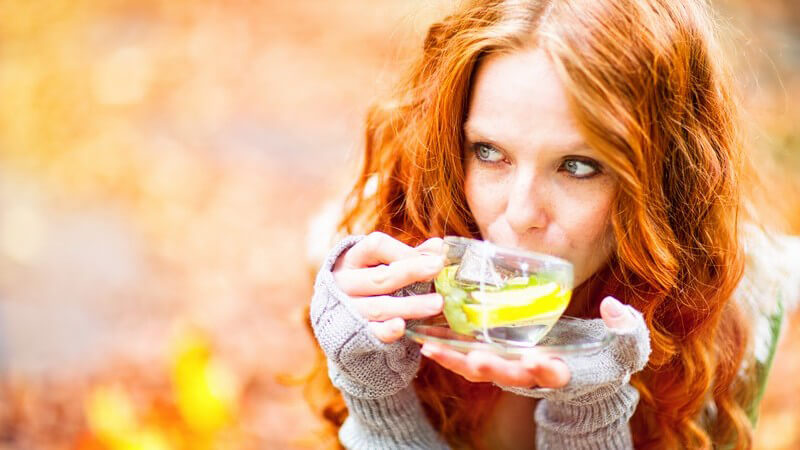 Junge Frau mit langen roten Locken trinkt einen Tee in der herbstlichen Natur