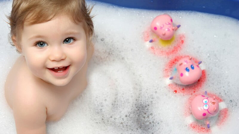 Kleines Mädchen in Baby-Badewanne mit Schaum, Spielzeug