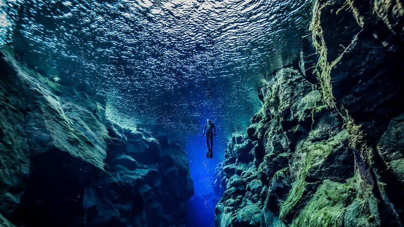 Große Felsen unter Wasser, in der Ferne ist ein Taucher zu sehen