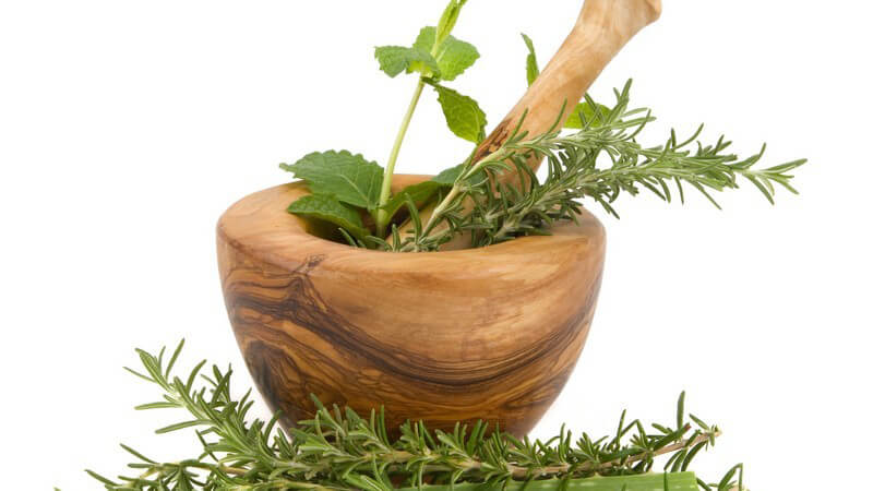 Grüne Kräuter vor und in Holzmörser