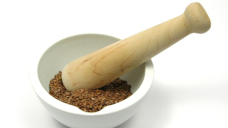 Leinsamen in weißer Schale mit Holzmörser auf weißem Hintergrund