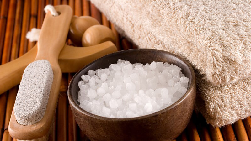 Badesalz, Bürste, Massagestab und Handtuch auf Bastmatte