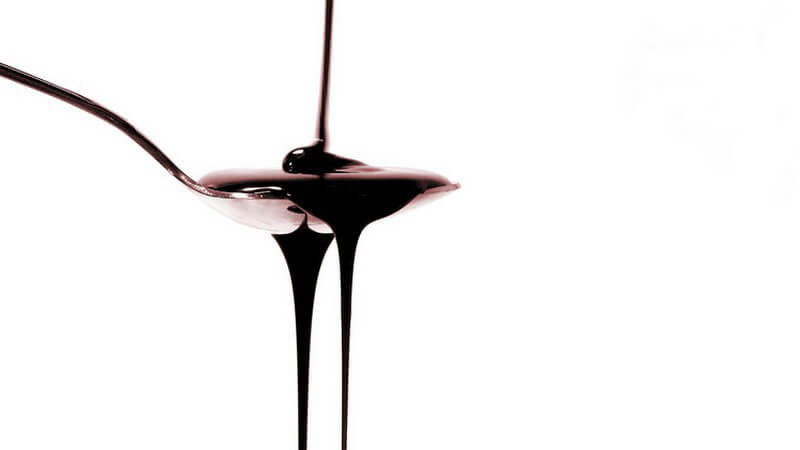 Löffel mit herunterlaufendem Schokoladen-Sirup vor weißem Hintergrund