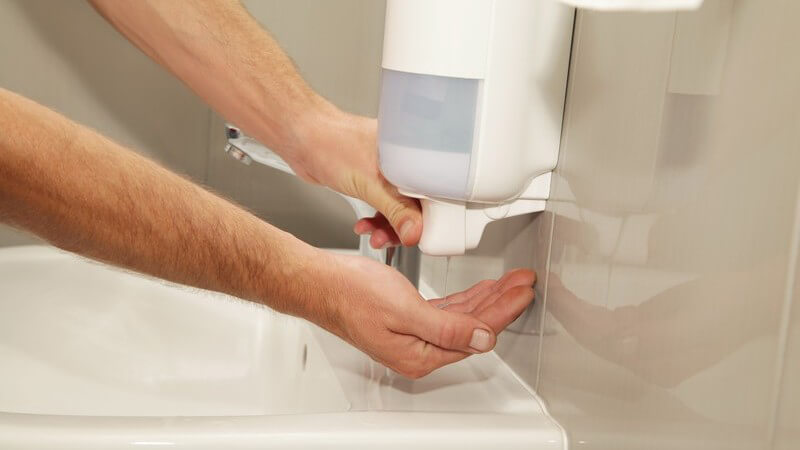 Mann nimmt zum Händewaschen Seife aus einem Seifenspender einer öffentlichen Toilette