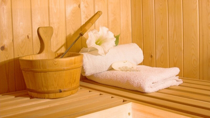 Saunaeimer mit Löffel, weißen Handtüchern und weißer Lilie auf einer Saunabank