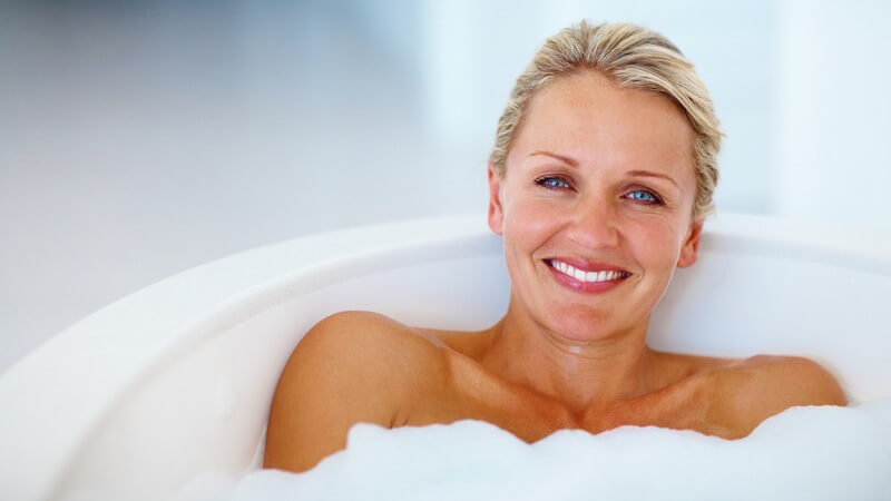 Frau liegt in Badewanne und lächelt in Kamera