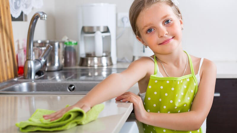 Mädchen in grüner Kochschürze putzt die Küche mit einem grünen Lappen