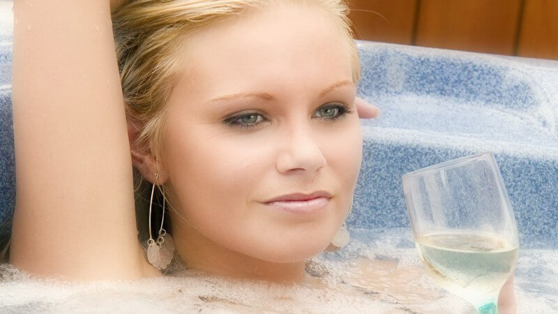 Junge blonde Frau mit Glas Weißwein relaxt im Whirlpool