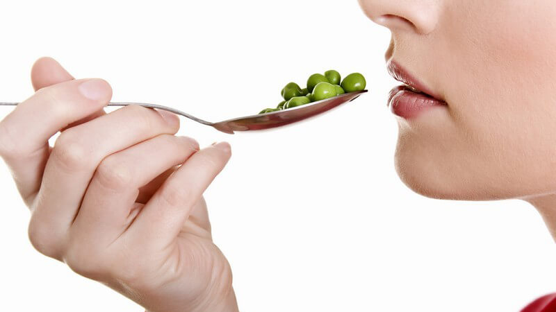 Junge Frau führt Löffel mit Erbsen zum Mund
