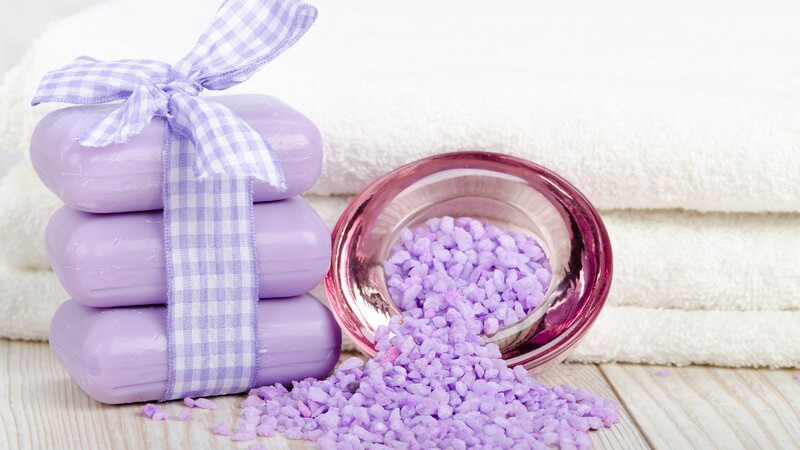 Lila Seifenstücke mit Schleife und Badesalz vor weißen Handtüchern