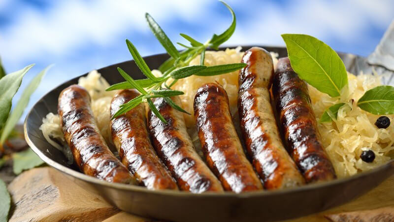 Rostbratwürste auf Sauerkraut in Eisenpfanne auf dickem Holzbrett