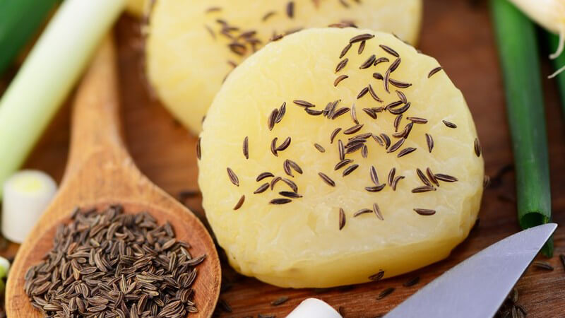 Kümmel auf Holzlöffel und Kartoffelscheiben