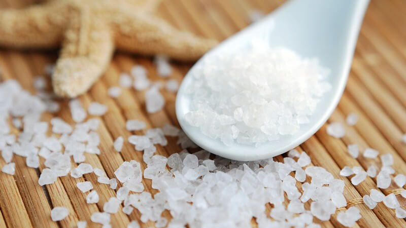 Grobes Salz in Löffel auf Bastmatte, daneben Deko Seestern