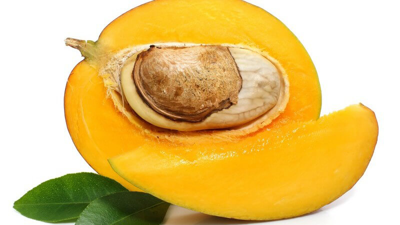 Frische halbierte Mango mit Kern und grünen Blättern auf weißem Hintergrund