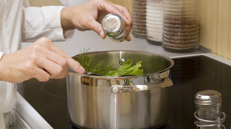 Topf mit Gemüse auf dem Herd wird aus Salzstreuer gesalzen