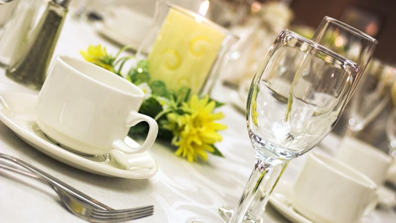 Nahaufnahme gedeckter Tisch mit Kaffeetassen, Besteck, Weingläsern und Kerzen