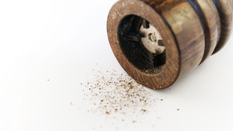 Unterseite einer Pfeffermühle, davor etwas gemahlener Pfeffer