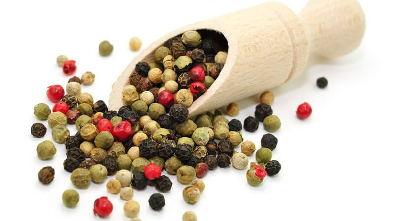 Bunte Pfefferkörner, teils in Holzlöffel, auf weißem Hintergrund
