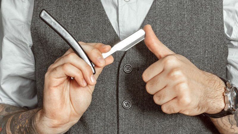 Barbier in grauer Weste testet die Schärfe des Rasiermessers mit seinem Finger