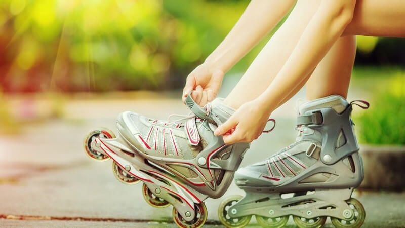 Frau sitzt im Sonnenlicht und zieht sich ihre grauen Inlineskates an