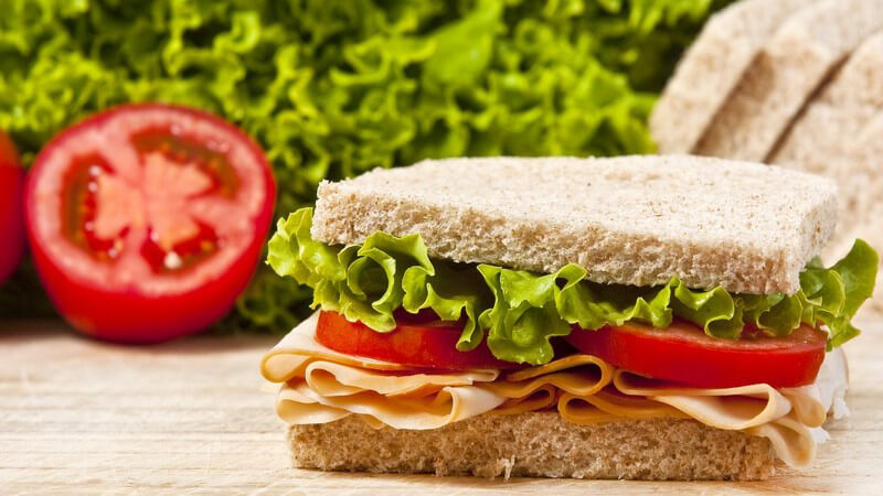 Sandwich mit Blattsalat, Tomate und Wurst - im Hintergrund Tomate, Salat und Brot