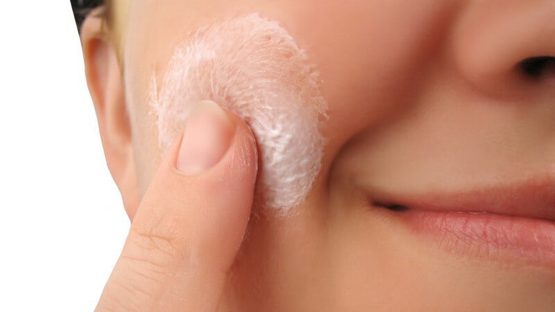 Nahaufnahme lächelndes Frauengesicht mit Hautcreme, die mit dem Finger eingecremt wird