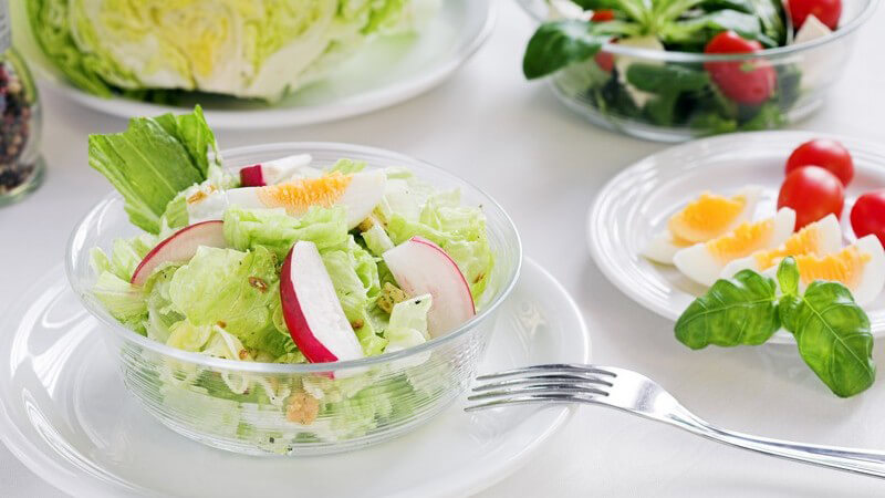 Schüssel mit zubereitetem frischen Salat, daneben gekochte Eier, Radieschen