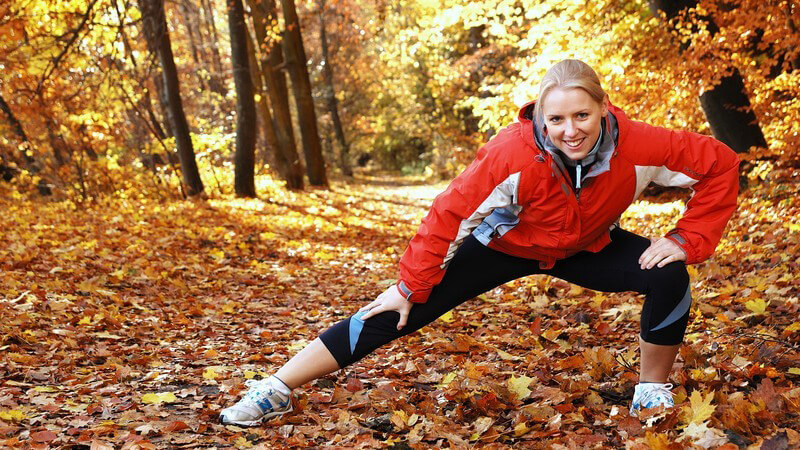Junge blonde Joggerin macht Dehnübungen im Wald, Herbsttag