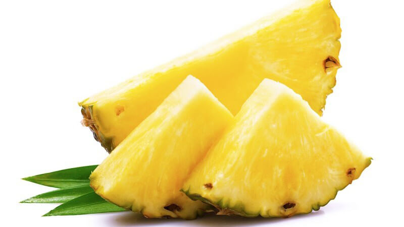 Eine halbe und zwei geviertelte Ananas-Scheiben vor weißem Hintergrund
