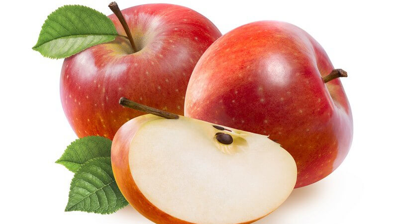 Zwei ganze und ein geviertelter Apfel der Sorte "Jonathan" vor weißem Hintergrund