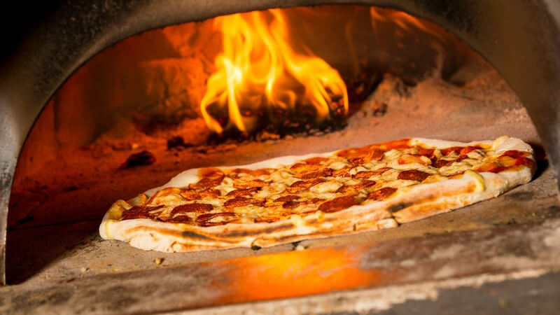 Salami-Pizza liegt in einem großen, mit Feuer beheiztem Pizzaofen