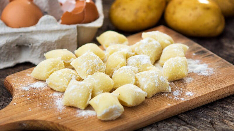 Selbstgemachte Gnocchi auf einem Holzbrettchen neben Eiern und Kartoffeln