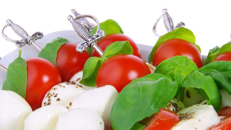 Spieße mit Mozarella, Tomaten, Basilikum auf Teller