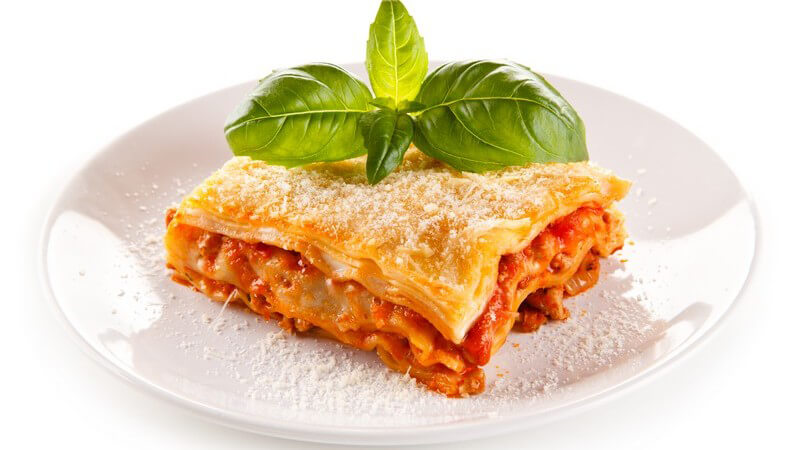 Teller mit einem Stück klassischer Lasagne, garniert mit Parmesan und Basilikum