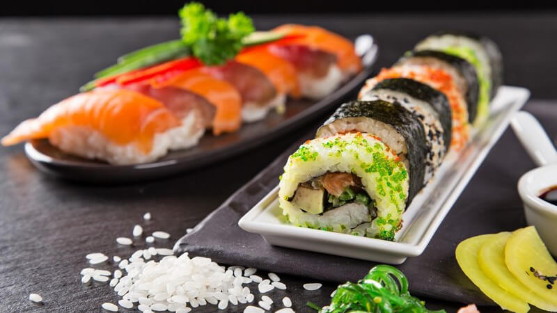 Sushi aus Fisch und Meeresfrüchten liegt sauber angeordnet auf zwei langen Platten