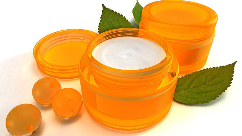 Zwei orangene Cremedöschen, daneben orange Badekugeln