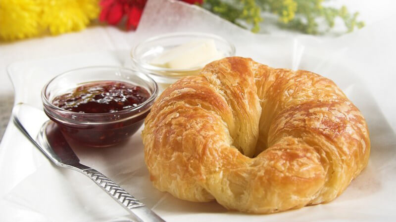 Frühstückstablett mit Croissant, Schälchen mit Marmelade und Quark, Messer, im Hintergrund Blumen