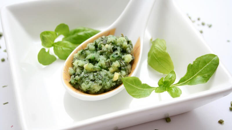 Basilikumpesto auf weißem Löffel über weißem Teller mit frischem Basilikum