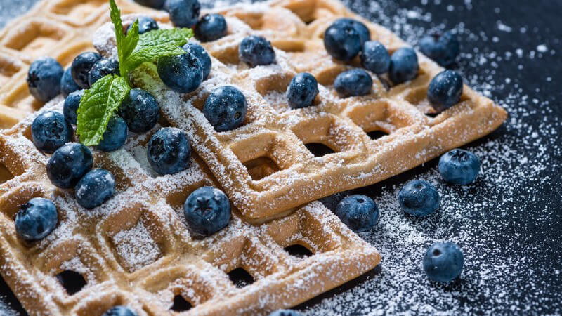 Belgische Waffeln mit Puderzucker und Blaubeeren auf dunklem Untergrund