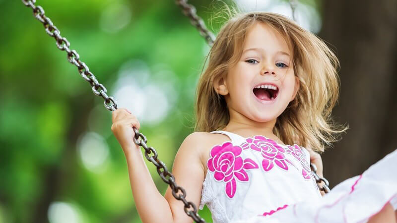 Mädchen in weißem Kleid mit pinken Blumen beim Schaukeln